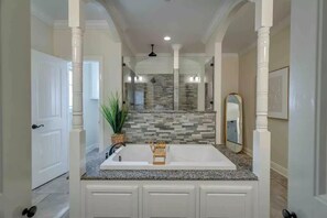 Une salle de bain avec un grand lavabo blanc, un comptoir en granit et un pare-feu en pierre.