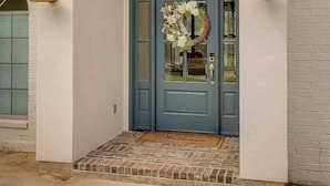 Blaue Haustür mit Kranz, Backstein trittstufe und zwei wandmontierten Leuchten.