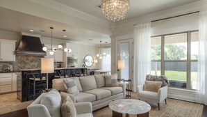 Ein geräumiges Wohnzimmer mit einer großen Couch, einem Couchtisch und einem Essbereich, im Hintergrund befindet sich eine Küche.
