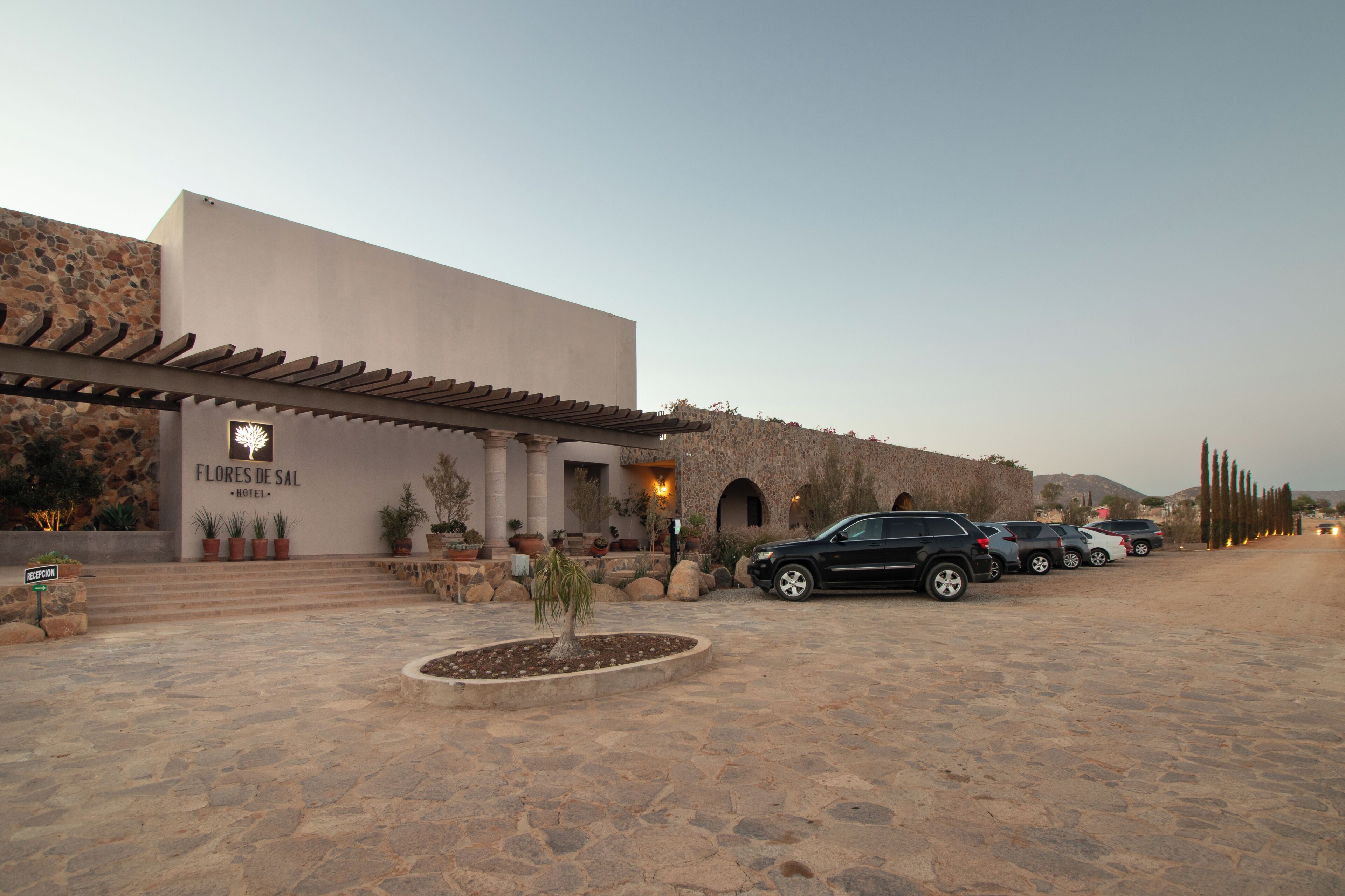 Un hotel con fachada de piedra, una zona de recepción y un estacionamiento con varios coches.
