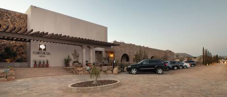 Un hotel con fachada de piedra, una zona de recepción y un estacionamiento con varios coches.