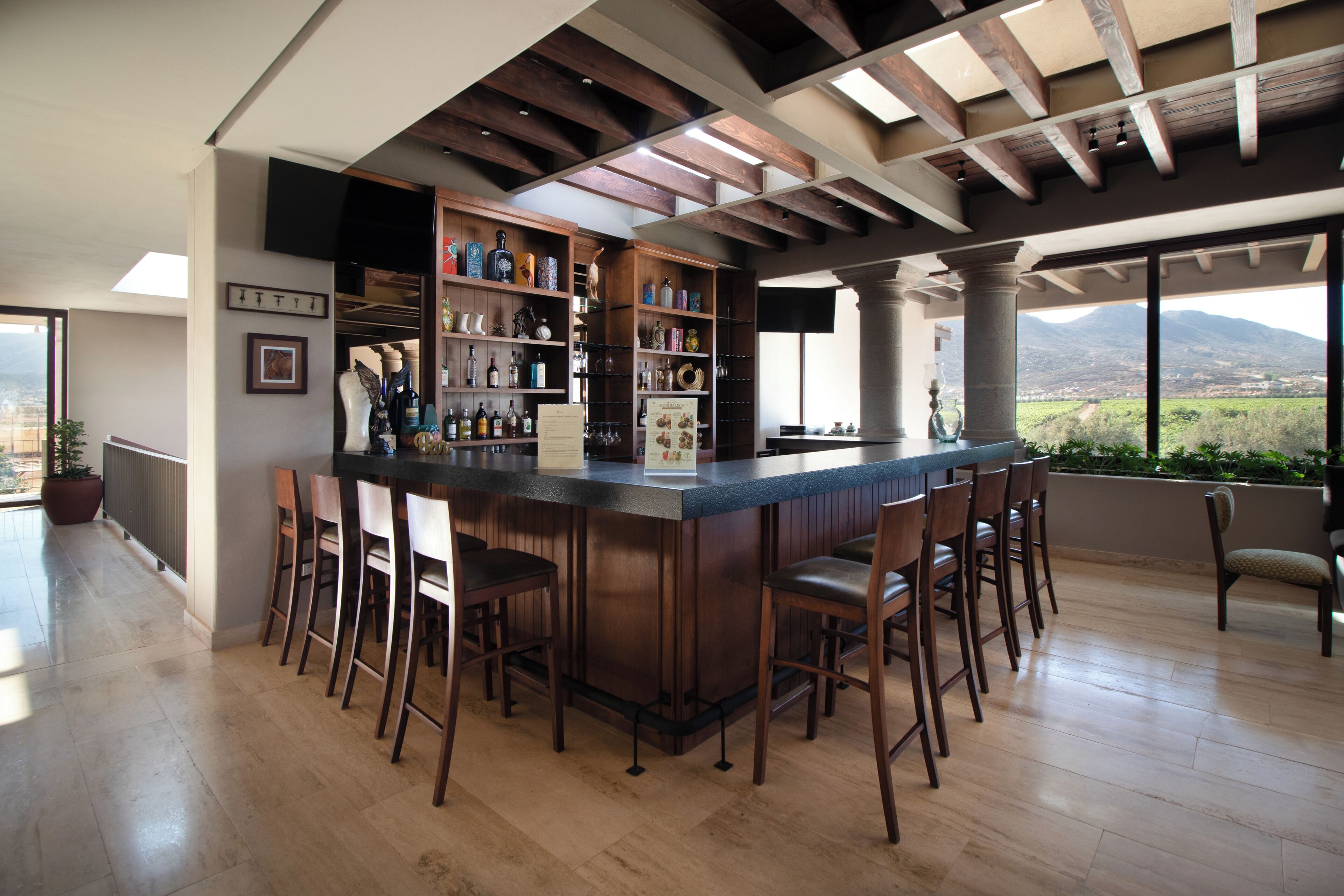 Un espace bar avec des chaises en bois, un comptoir et des étagères remplies de bouteilles et de verres.