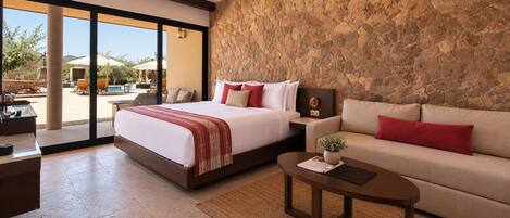 A hotel room with a bed, a sofa, a coffee table, and a stone wall.