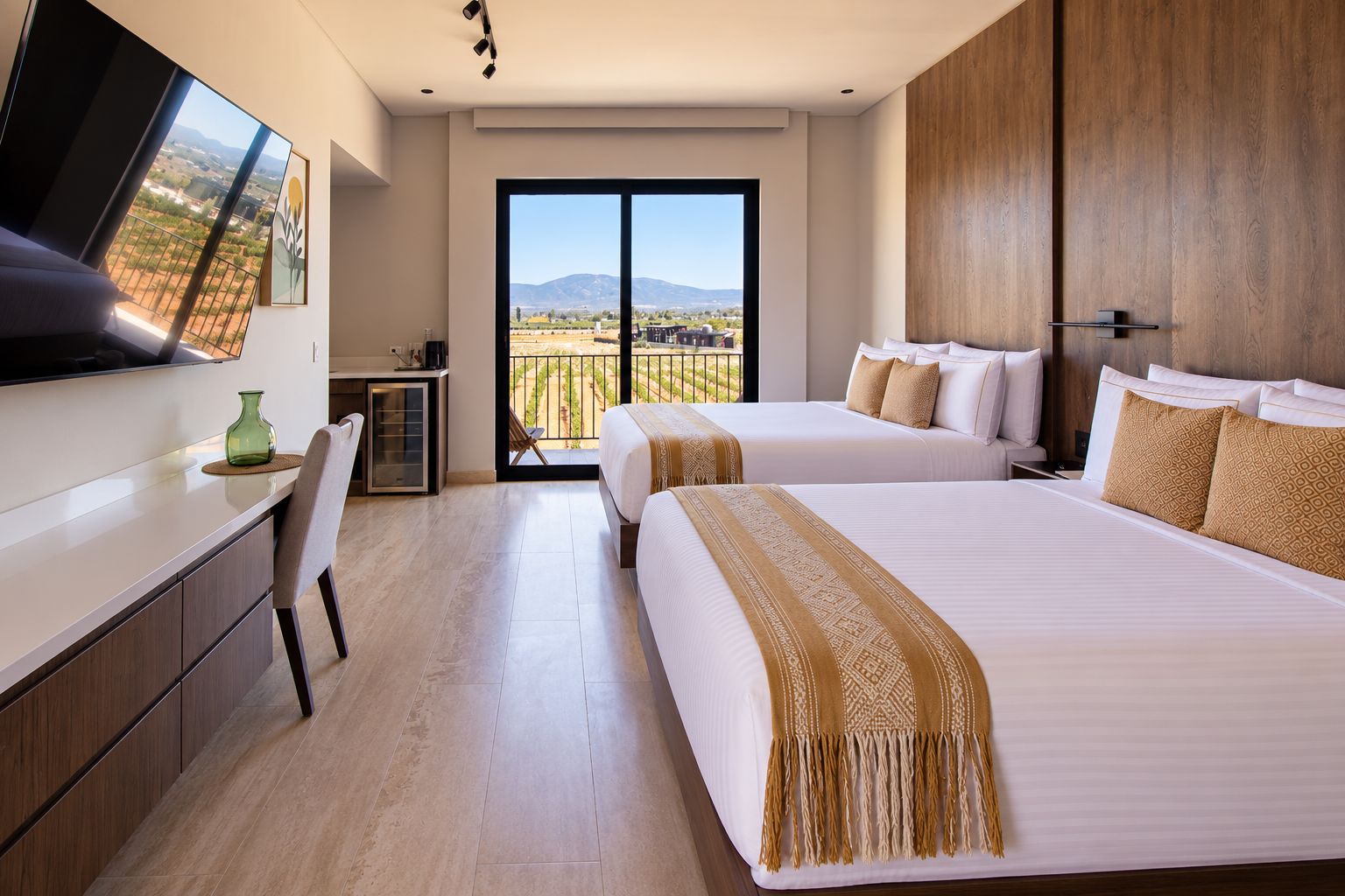 A hotel room with two beds, a desk, a chair, and a large window offering a view of the countryside.