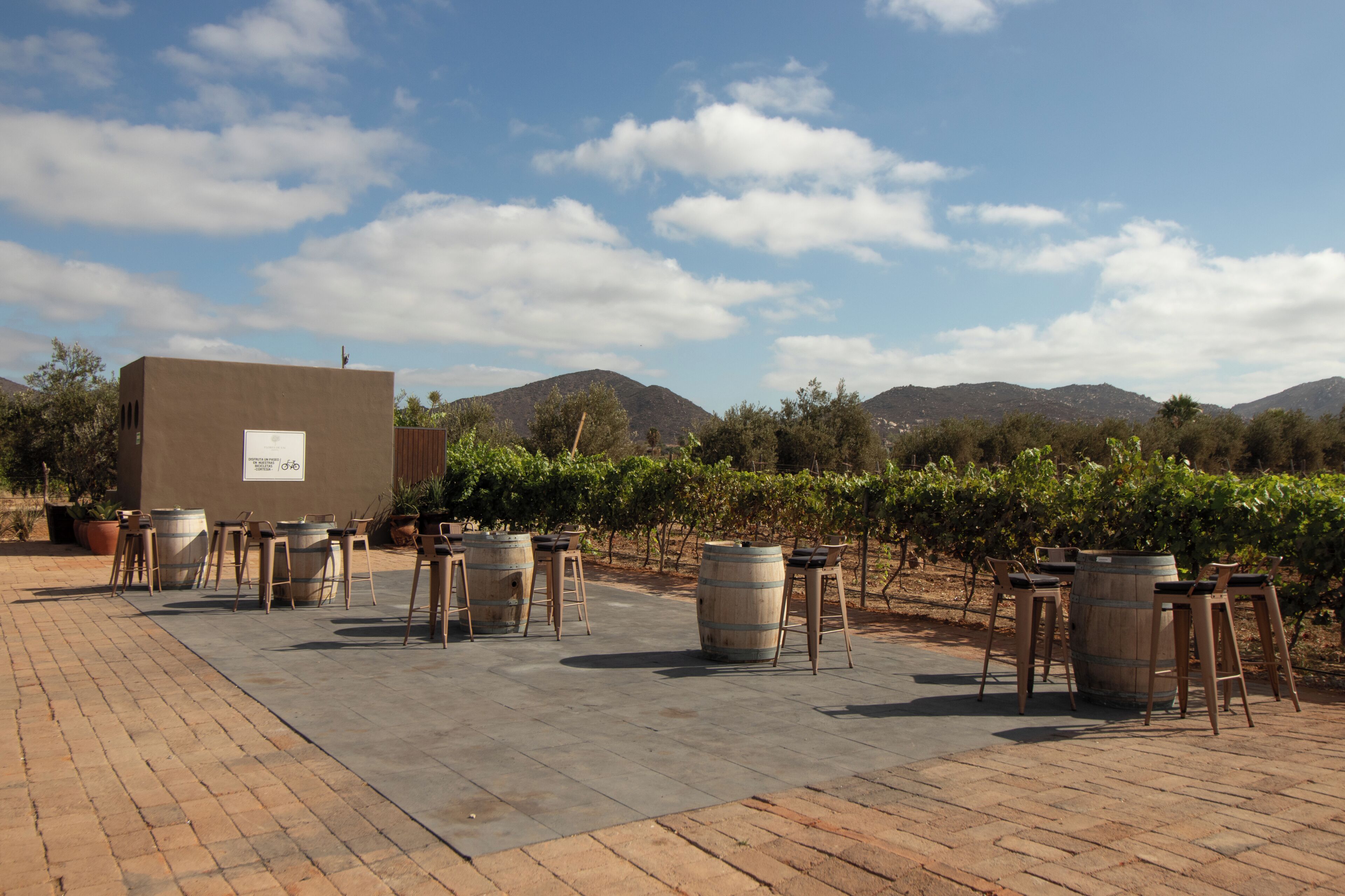 Un espacio al aire libre con mesas y sillas, un barril de vino y un letrero que indica una zona de estacionamiento para bicicletas.