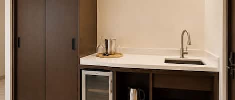 A compact kitchenette with a built-in fridge, a sink, and a coffee machine.