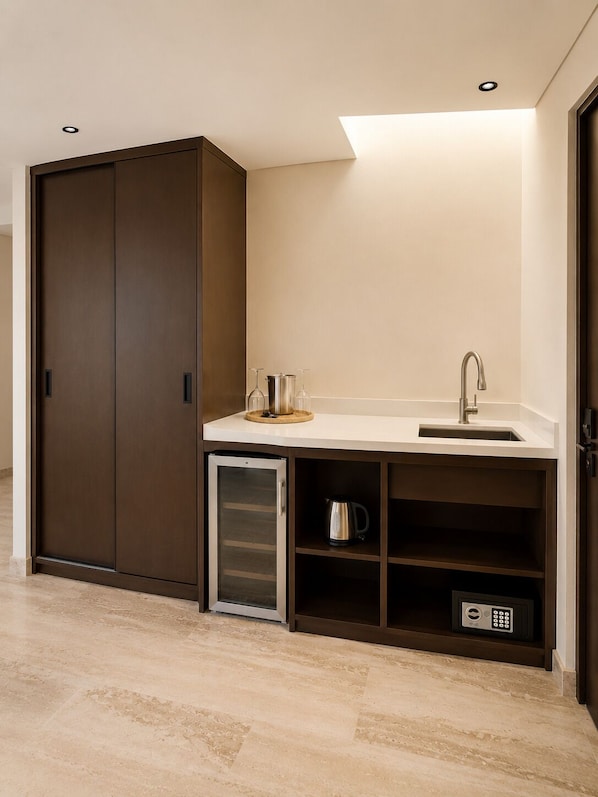 Una kitchenette compacta con nevera integrada, un lavamanos y una cafetera.