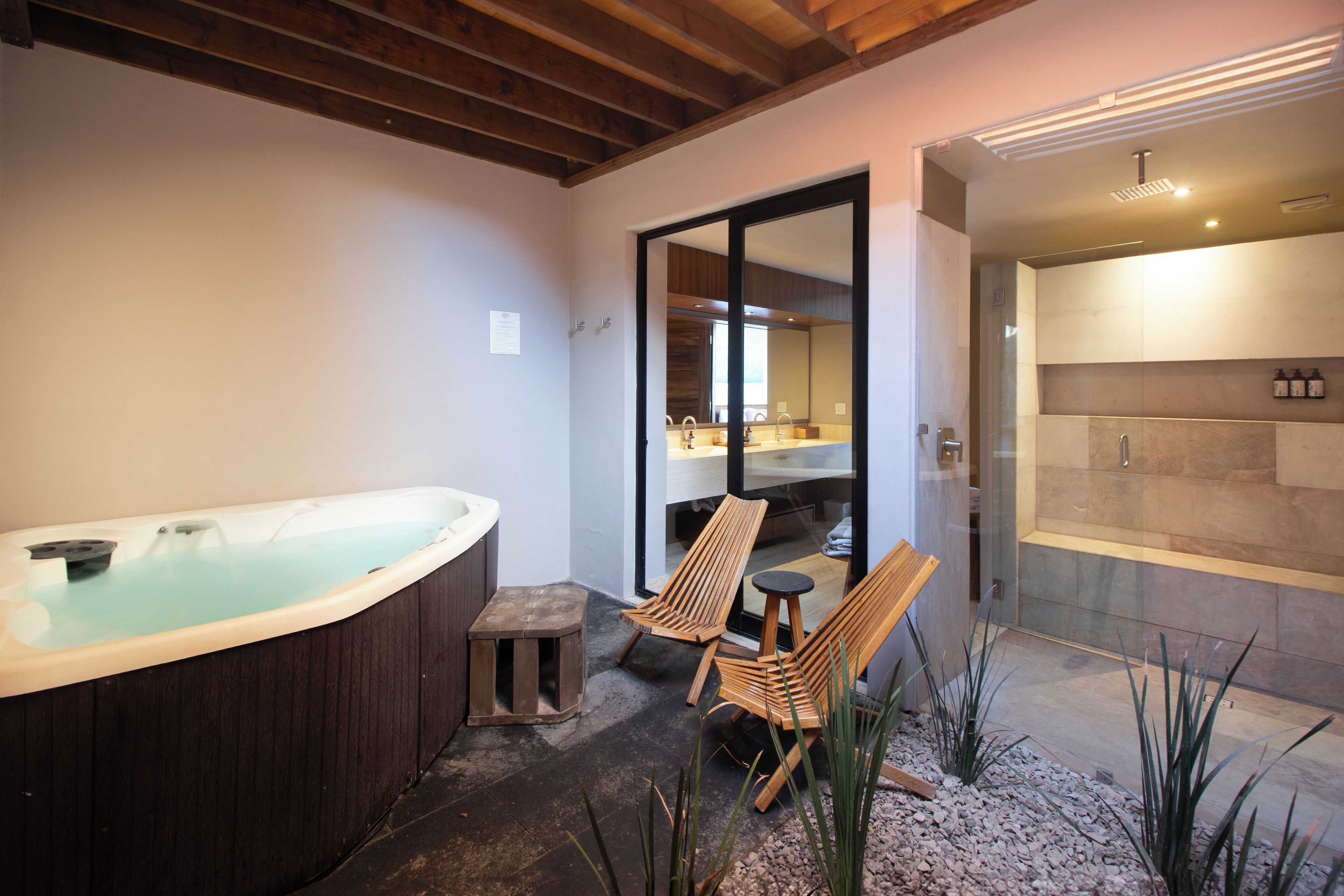 Un área de spa con un jacuzzi, dos sillones de madera y una ducha con cerramiento de vidrio.