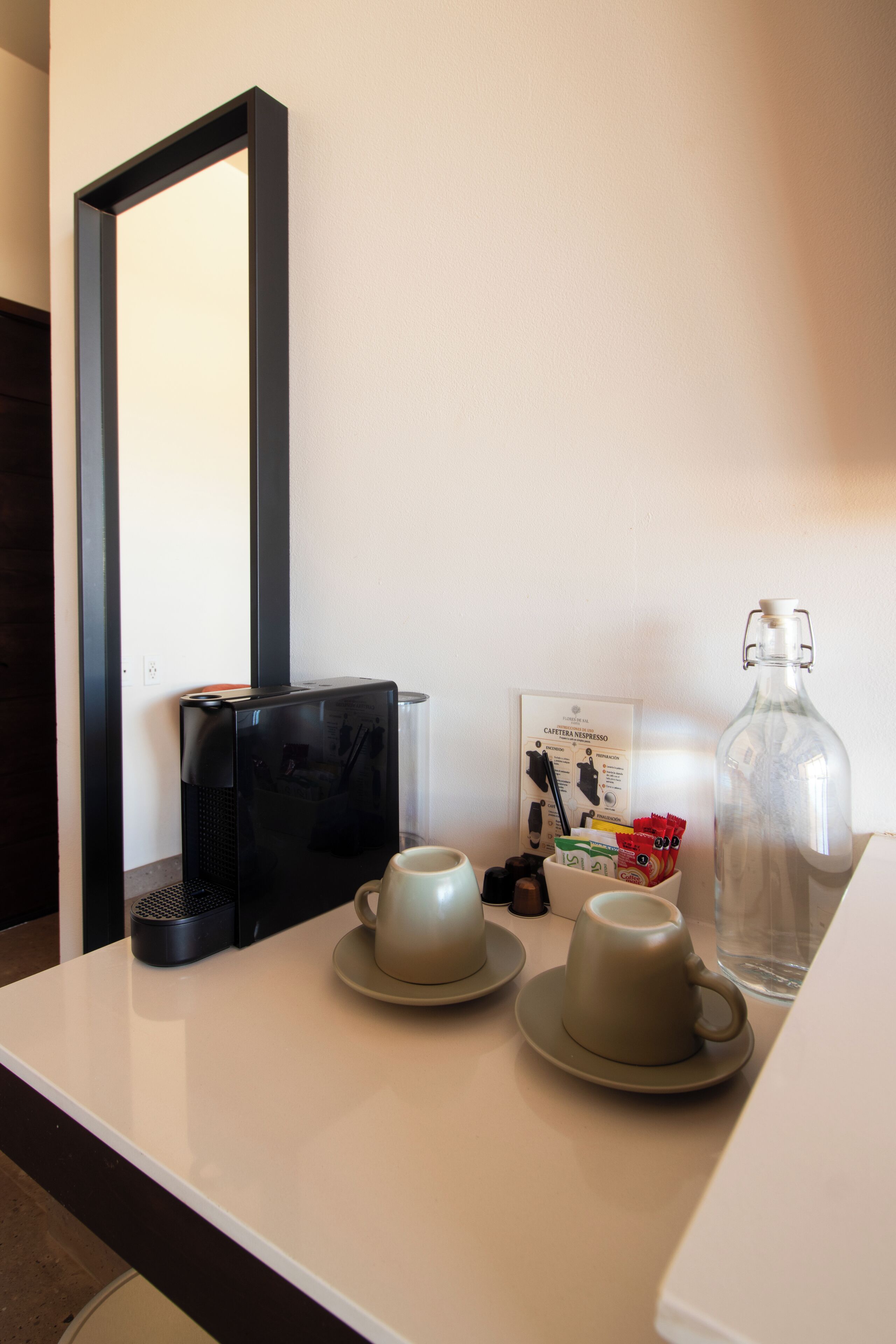 Una mesa ordenada con una cafetera, dos tazas, una botella de vidrio y un menú.