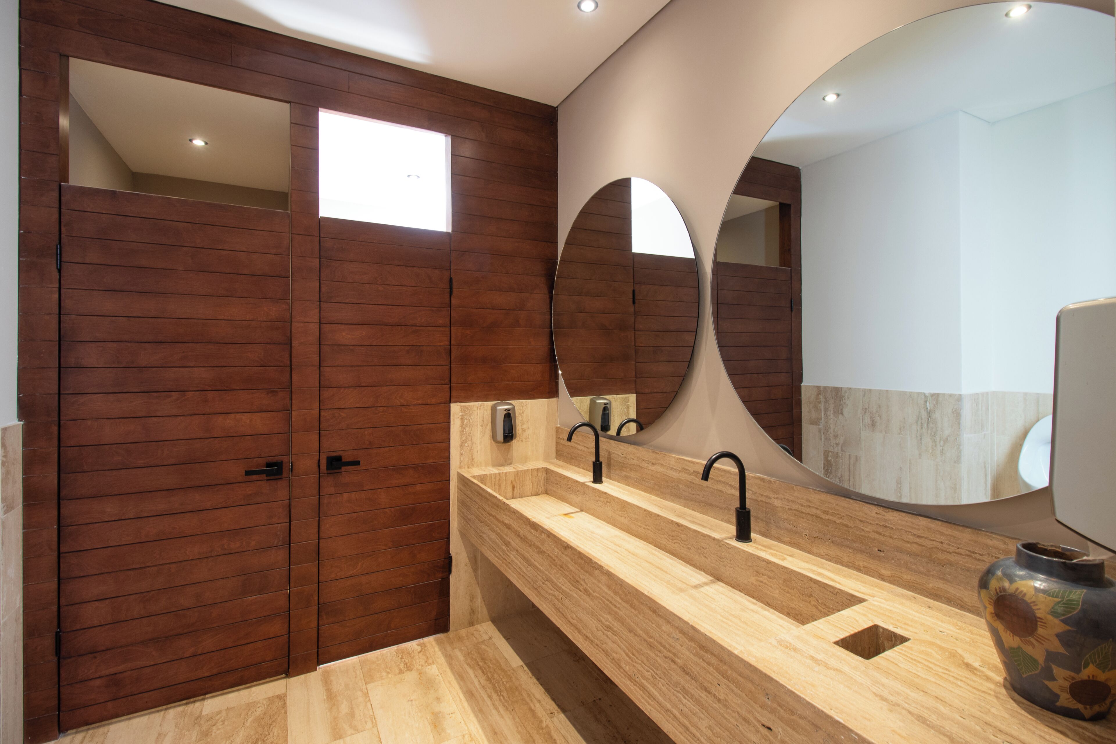 Un baño moderno con paneles de madera, un espejo grande y un tocador de madera con un florero.