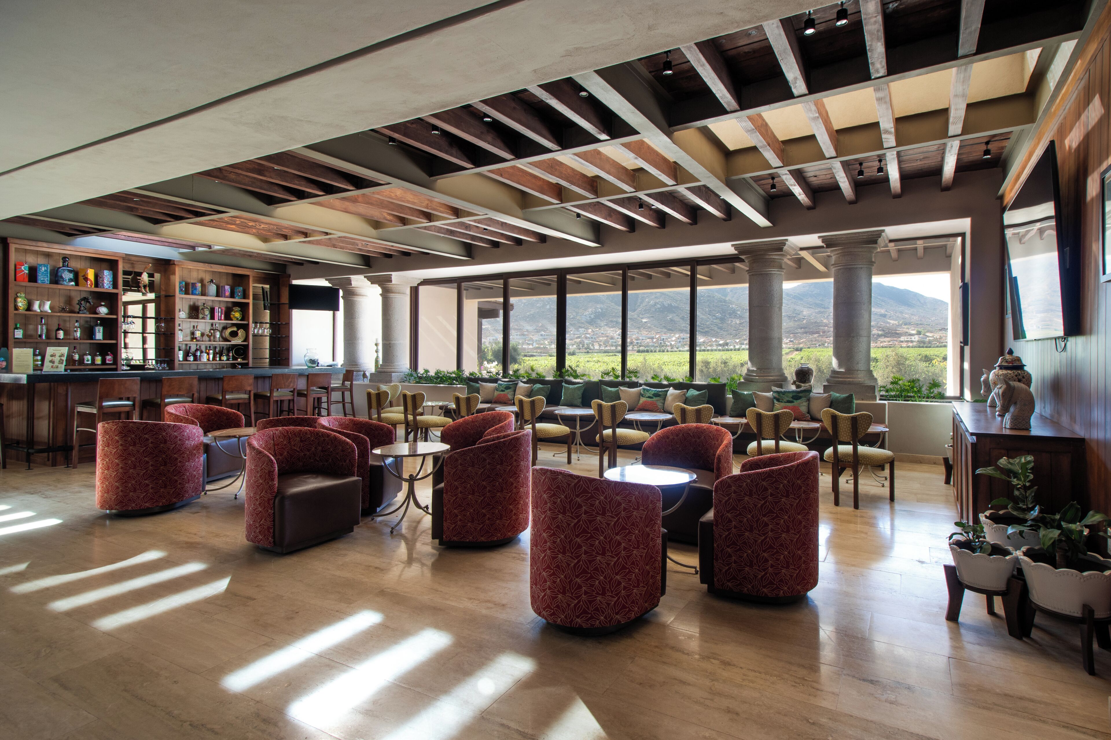 A spacious lounge area with multiple seating options, a bar with a variety of bottles, and large windows offering a view of the landscape.