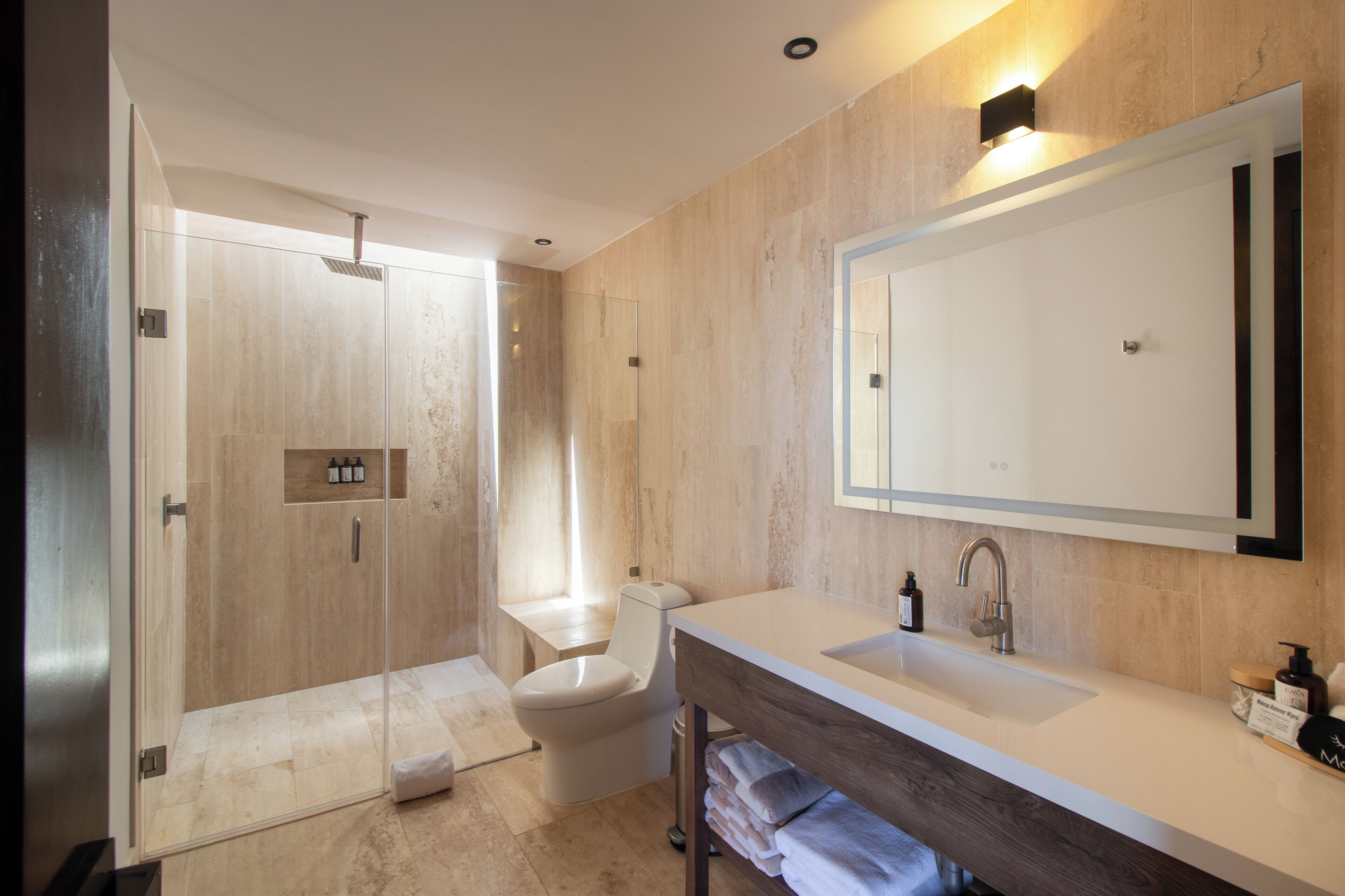 A modern bathroom with a glass-enclosed shower, a toilet, and a vanity with a large mirror.