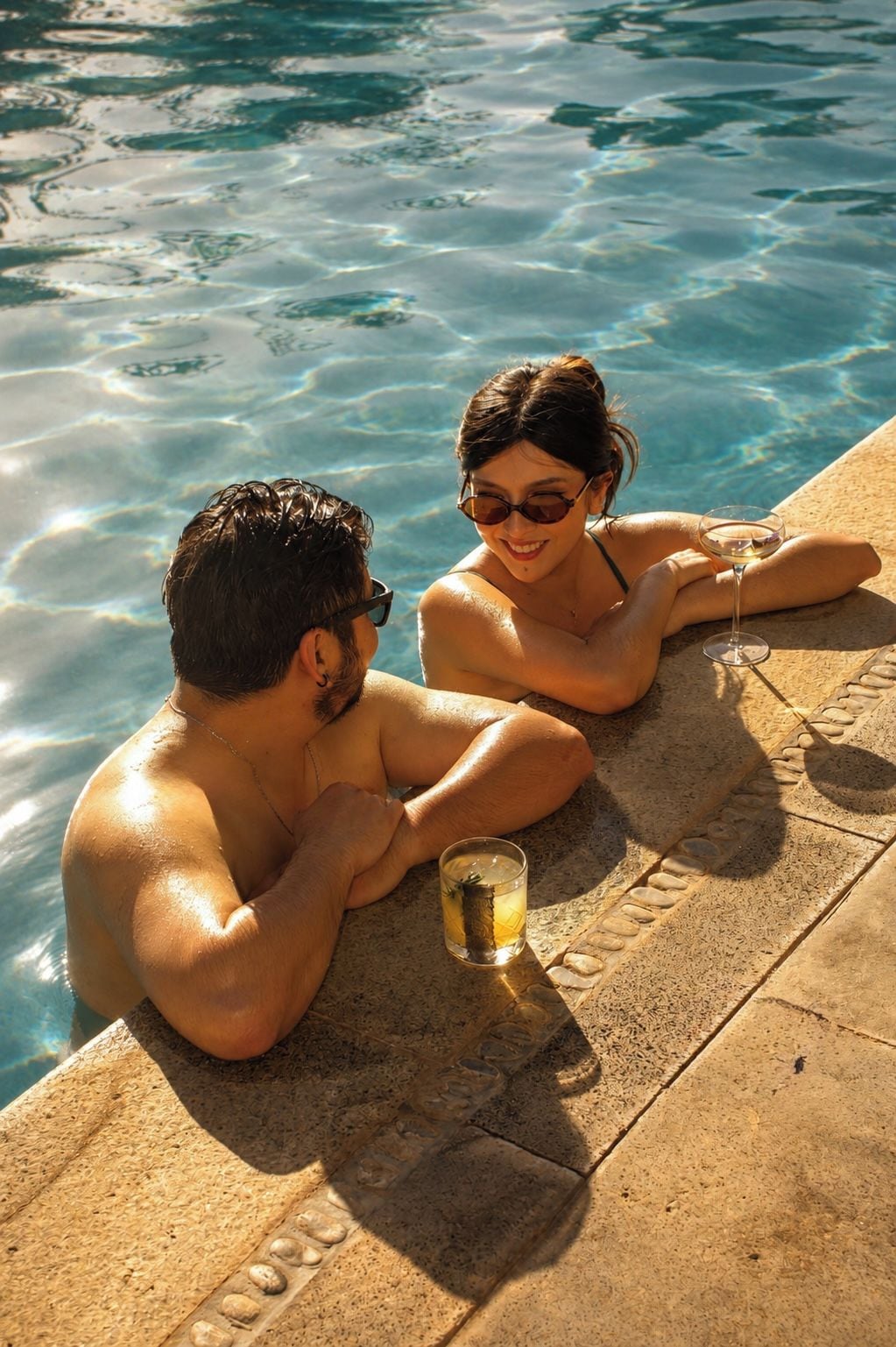 Two people sitting by a poolside with a drink in hand.