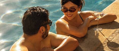 Two people sitting by a poolside with a drink in hand.