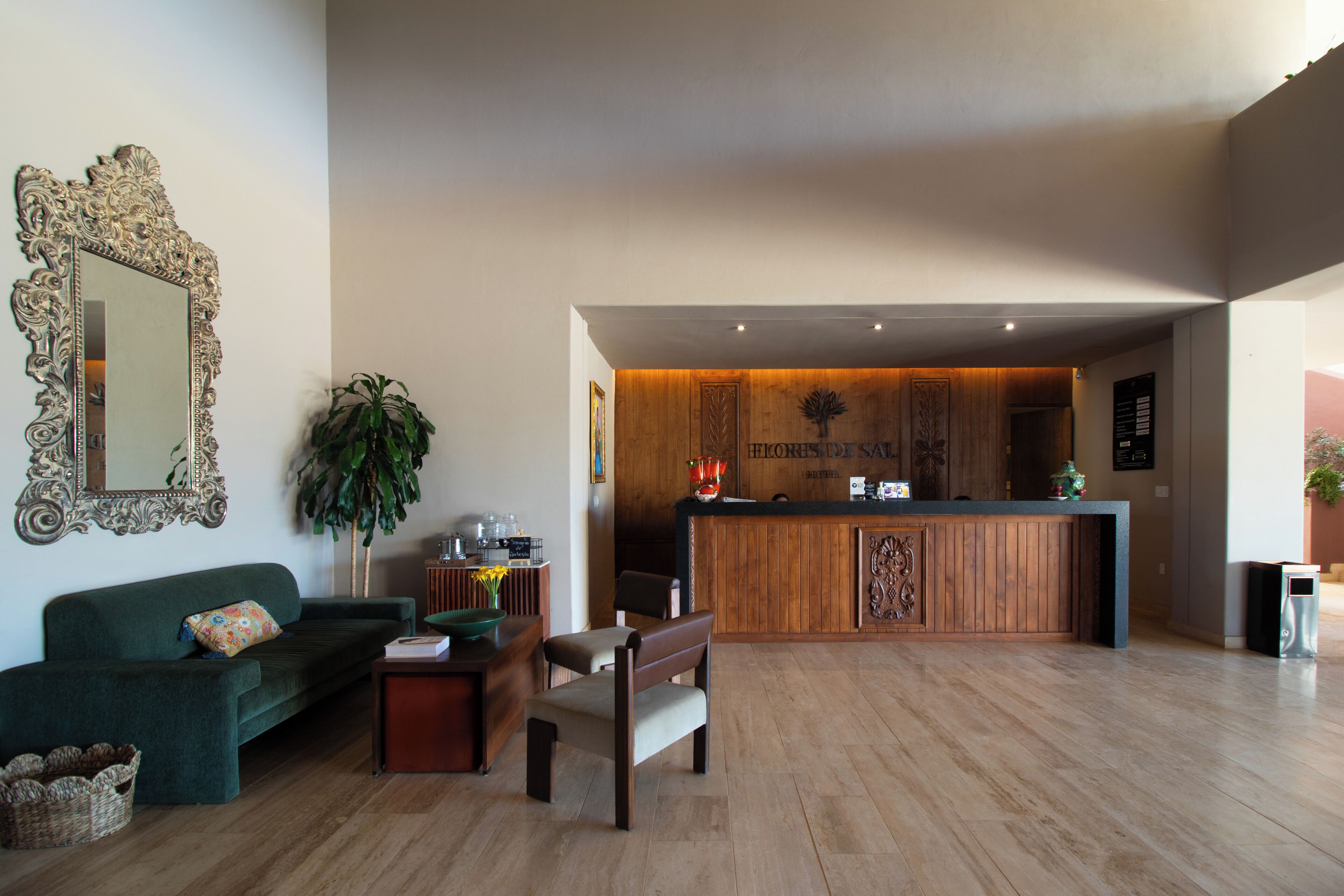 Una hall d'albergo con una reception, un divano verde, una panca e un grande specchio.