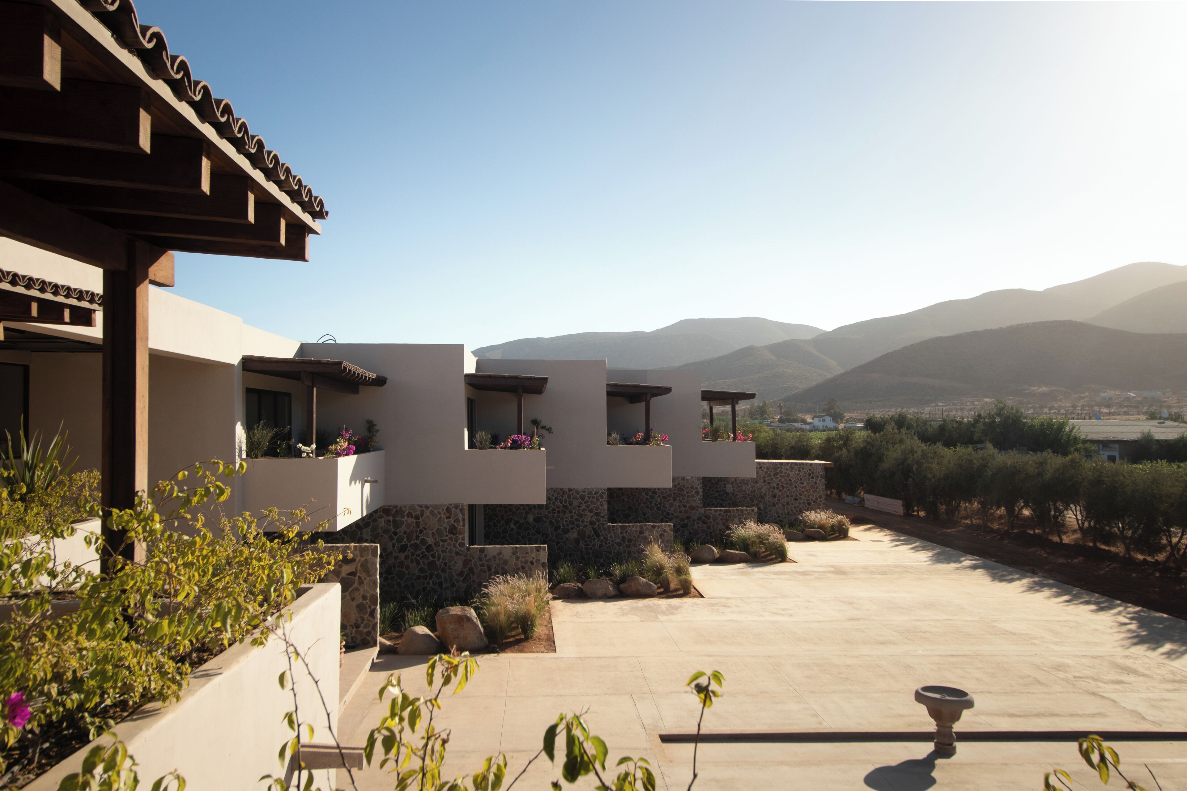 A modern building with multiple balconies overlooking a landscaped area with mountains in the background.