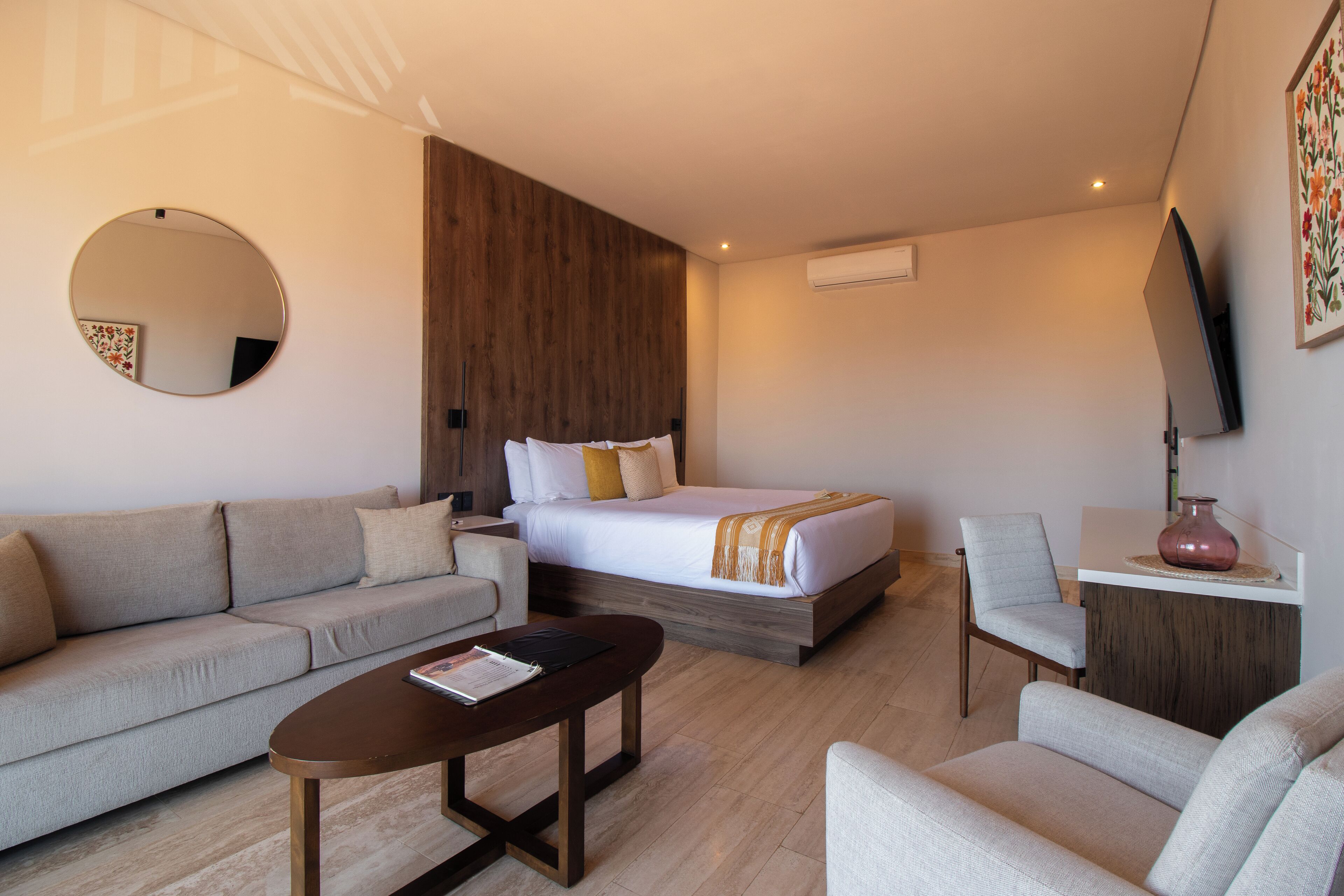 A modern hotel room with a bed, sofa, armchair, coffee table, and a flat-screen TV.