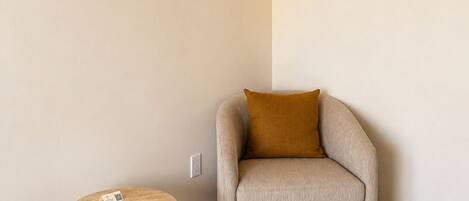 A room with a round wooden table, a beige armchair with a brown cushion, and a light-colored wall.
