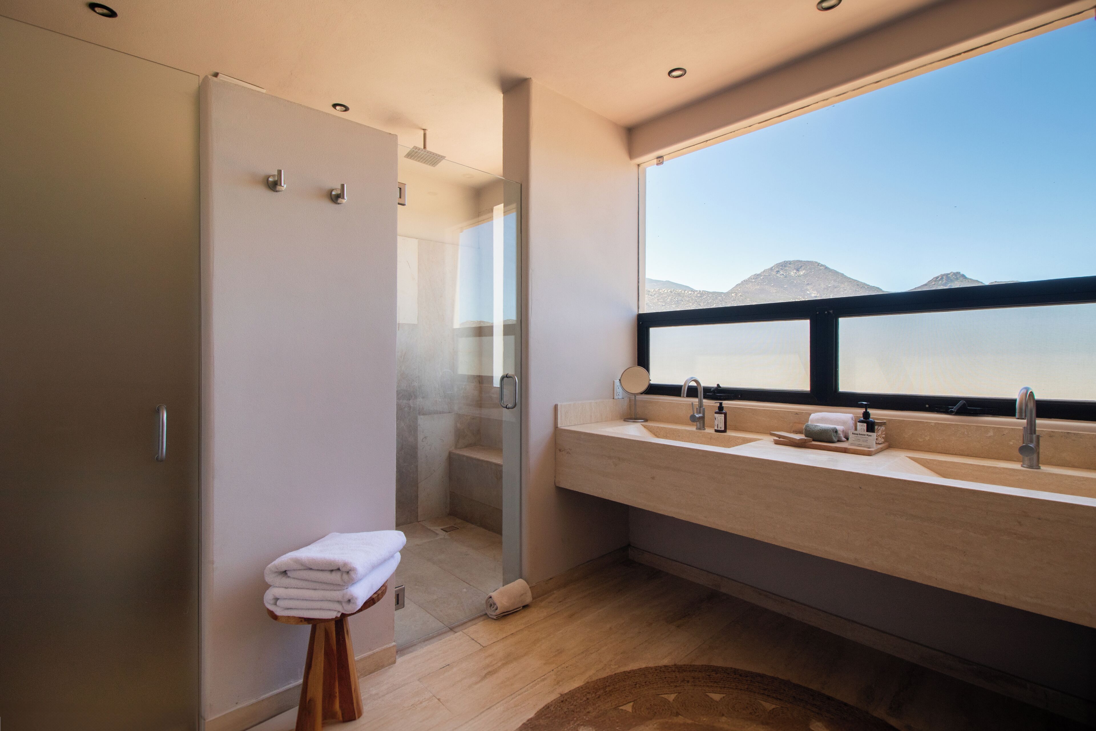 A modern bathroom with a large window, a shower, and a vanity with a mirror.