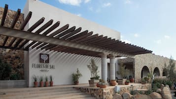 Entrada de un hotel con una pérgola, paredes de piedra y plantas en macetas.