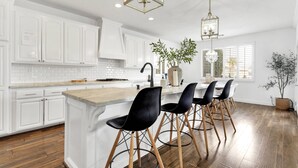A modern kitchen with white cabinetry, a wooden island, black bar stools, and pendant lighting.