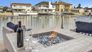 A patio with a fire pit, a bottle of wine, and glasses on a table.