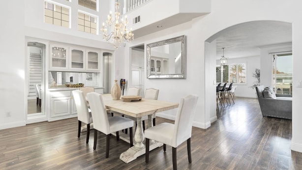 A spacious dining area with a large wooden table, white chairs, and a chandelier.