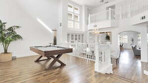 A spacious room with a pool table, wooden flooring, and a balcony with white railings.