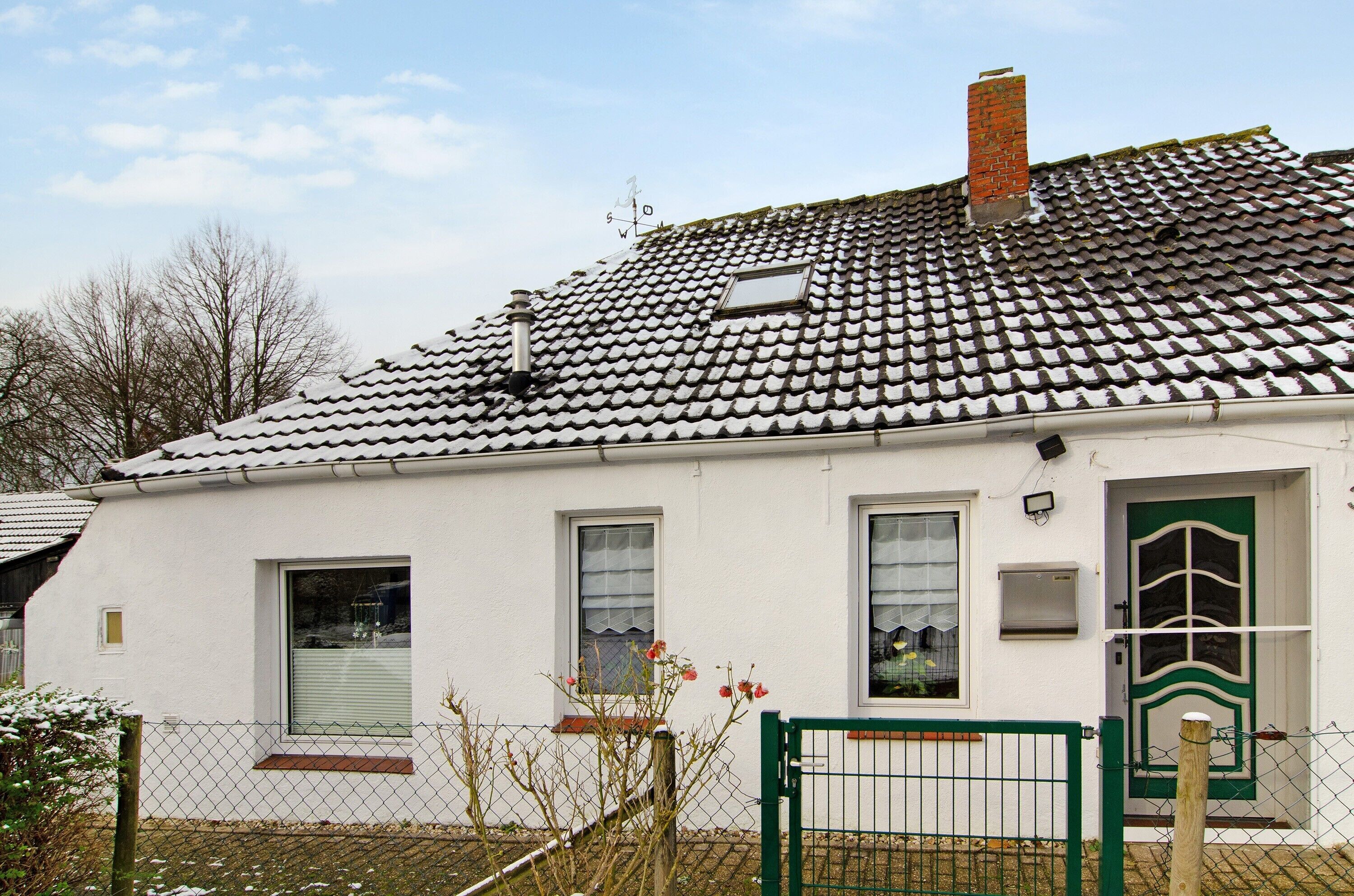 Ein weißes Gebäude mit einem Ziegeldach, einer grünen Tür und einem kleinen Fenster.