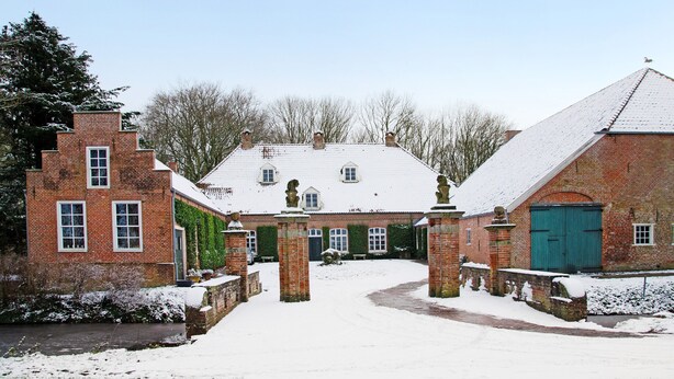 Een bakstenen gebouw met een sneeuwbedekte dak, een groene deur en een met baksteen bestraatte looppad die naar de ingang leidt.