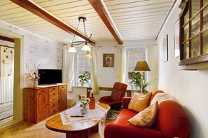 Un salon comprenant un meuble en bois, un téléviseur, un canapé rouge, une table avec un vase et une fenêtre avec des rideaux.