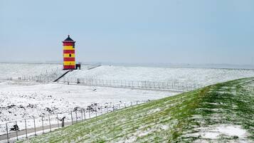 A lighthouse with a red and yellow striped tower, a snow-covered grassy area, and a clear sky.