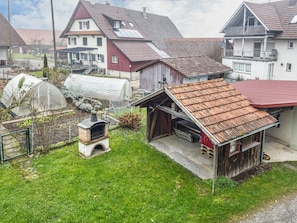 A residential area with a house featuring a red roof, a small outdoor oven, and a greenhouse.