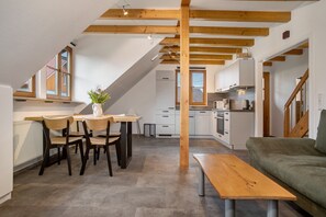 A modern kitchen with wooden beams, a dining area with chairs and a table, and a green sofa.