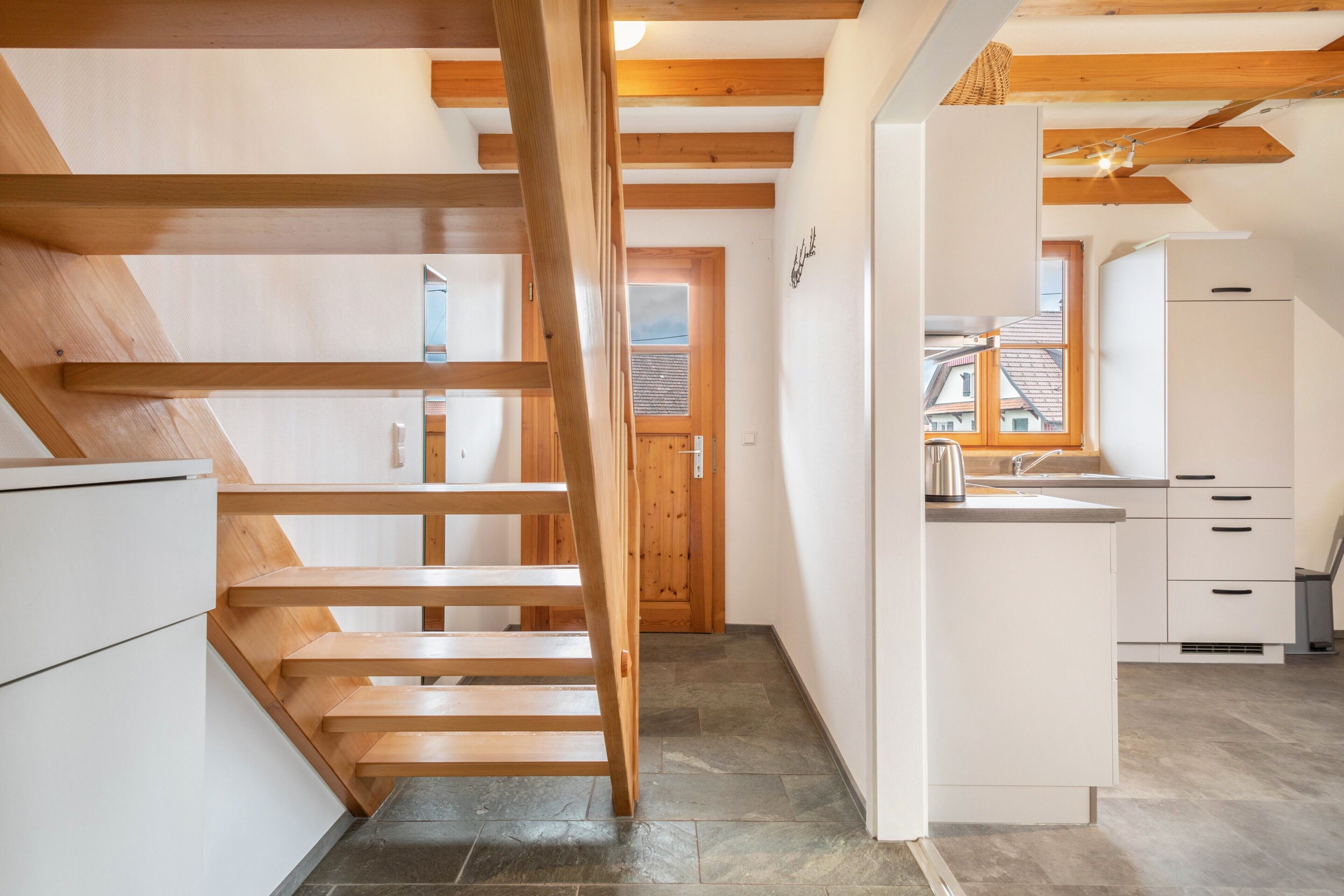 Una cocina moderna con armarios blancos, una escalera de madera y vistas al exterior.