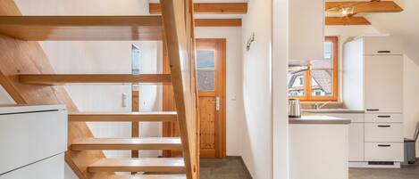 Una cocina moderna con armarios blancos, una escalera de madera y vistas al exterior.