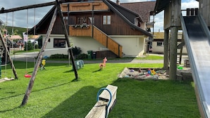 En legeplads med gynger og rutchebane, et træhus med balkon og et græsstykke.