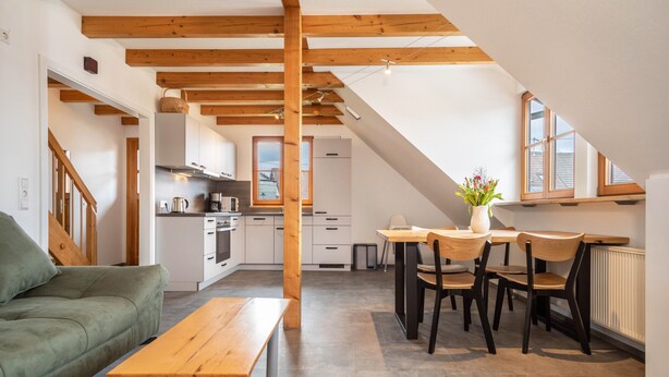 Et moderne køkken med træbjælker, et spiseområde med bord og stole, og en grøn sofa.