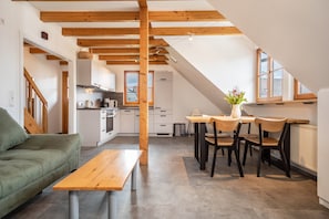 Une cuisine moderne avec des poutres en bois, un coin repas avec une table et des chaises, et un canapé vert.