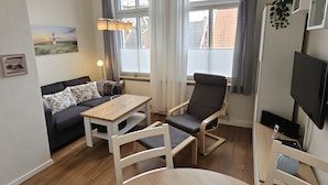 A room with a sofa, a table, a chair, a TV, and a window with curtains. - Apartment 'Hiddes Hus - Fuhrmann' with Wi-Fi (Borkum)
