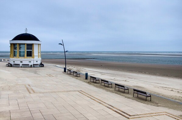 Un paseo marítimo con un pequeño quiosco, bancos y una vista despejada del mar.