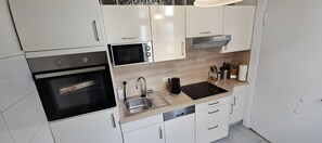 Una cocina moderna con armarios blancos, horno empotrado, microondas, pileta de acero inoxidable y cafetera.