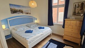 A bedroom with a bed, bedside lamps, a dresser, a window with curtains, and wall art. - Apartment 'Hiddes Hus - Fuhrmann' with Wi-Fi (Borkum)