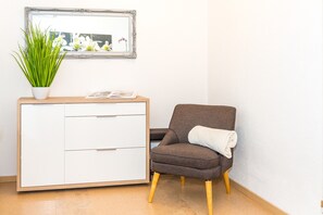 Une pièce avec un meuble blanc, une chaise marron avec un coussin blanc, une plante en pot et un miroir au mur.