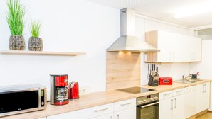 A modern kitchen with white cabinets, a stainless steel oven, a microwave, a red coffee maker, and two potted plants on a wooden shelf. - Holiday Apartment 'NaturPur' – Spacious, Quiet, Family-Friendly Retreat (Rheinau)