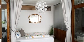 A bedroom with a bed, a mirror, a hanging light fixture, and a window with blinds.