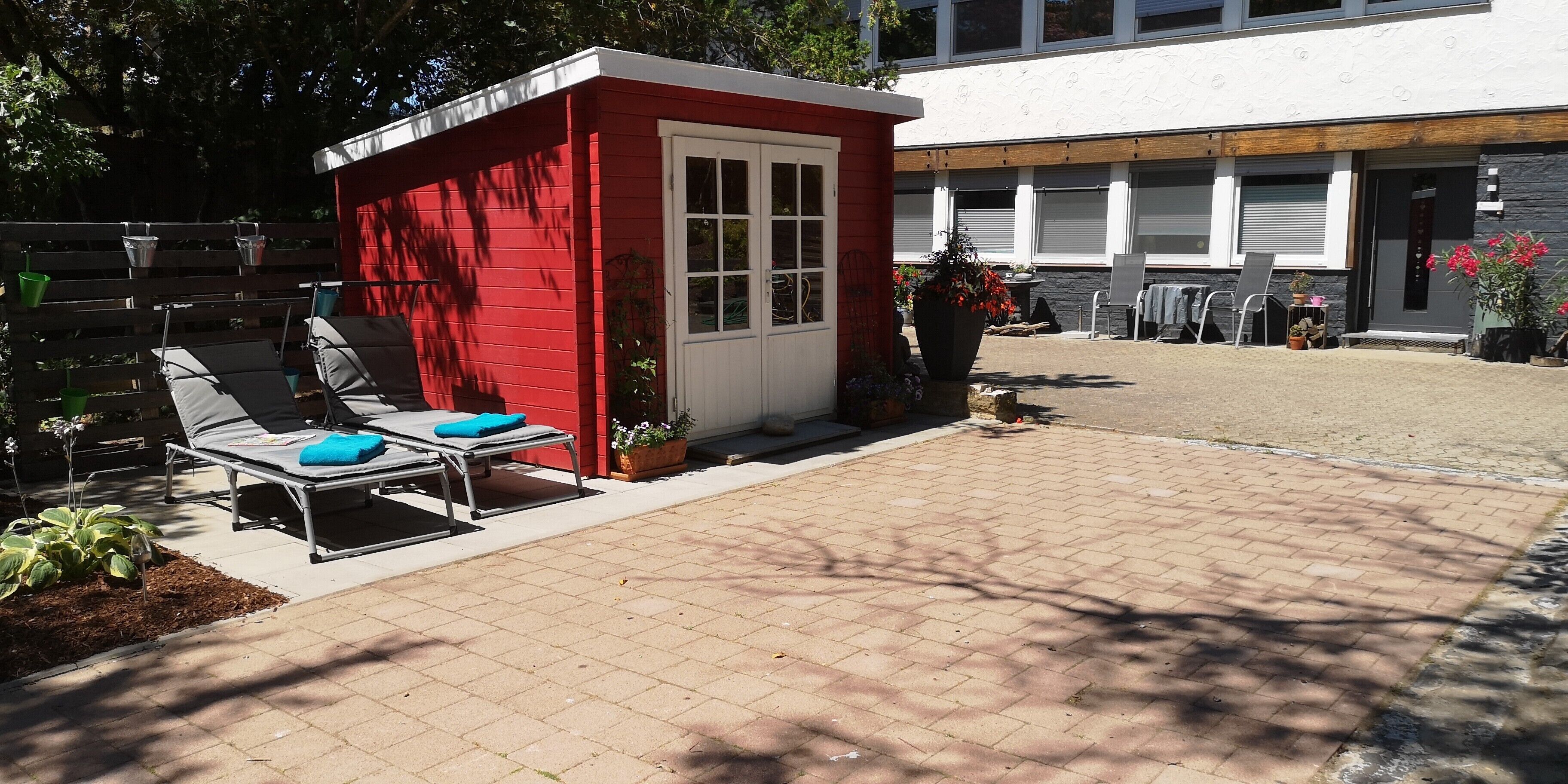 Un espace extérieur rouge, aménagé avec des fauteuils de jardin et un petit abri.