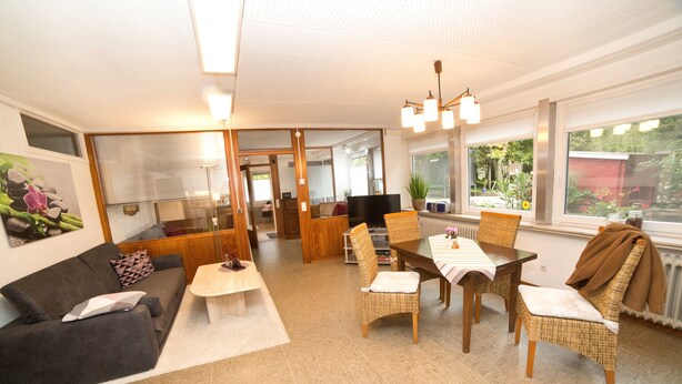 A modern living room with a sofa, dining table, chairs, and a TV. - Holiday Apartment 'NaturPur' – Spacious, Quiet, Family-Friendly Retreat (Rheinau)