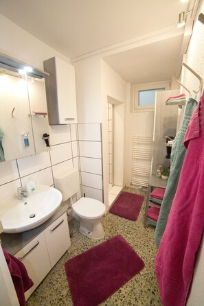 A bathroom with a white sink, toilet, and mirror, with pink and green towels on racks.