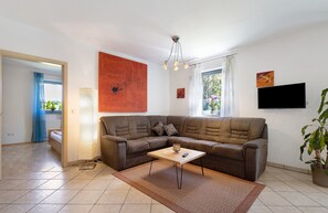 A living room with a brown sofa, a coffee table, a TV, and a large window with curtains. - Apartment 'Ferienwohnung Walter' with Private Terrace, Shared Garden and Wi-Fi (Plößberg-Wildenau)